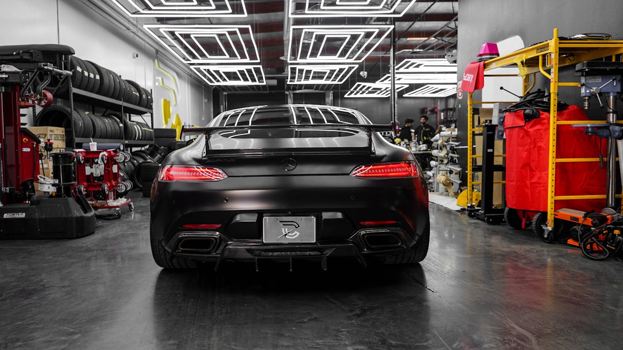 services-06 Rear view of a sleek black Mercedes Benz AMG GT in a modern, well-lit garage setting.
